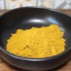 Poudre d'épices jaune vif dans un bol noir, idéale pour la cuisine exotique et recettes savoureuses.